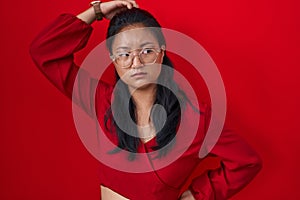 Asian young woman standing over red background confuse and wondering about question