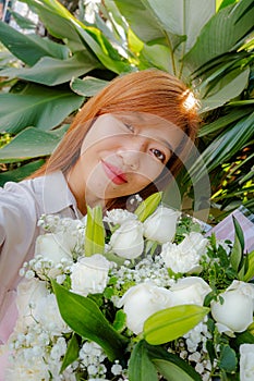 Asian young woman take a selfie and smiling with a big bouquet of white roses and lily flowers in the garden