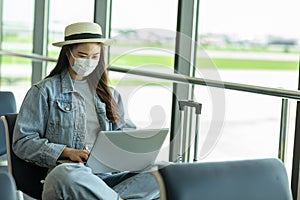 Asian young woman traveller wearing face maks using laptop computer at airport Due Covid-19 flu virus pandemic photo