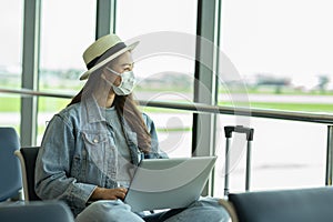 Asian young woman traveller wearing face maks using laptop computer at airport Due Covid-19 flu virus pandemic photo