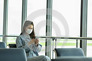 Asian young woman traveller wearing face maks using mobile phone at airport