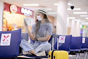 Asian young woman traveller wearing face maks using mobile phone at airport