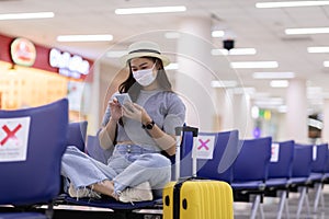 Asian young woman traveller wearing face maks using mobile phone at airport