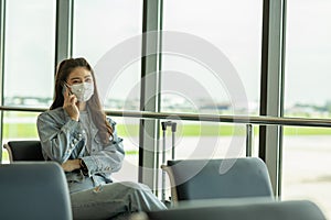 Asian young woman traveller wearing face maks using mobile phone at airport