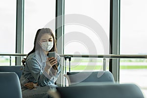 Asian young woman traveller wearing face maks using mobile phone at airport Due Covid-19 flu virus pandemic photo