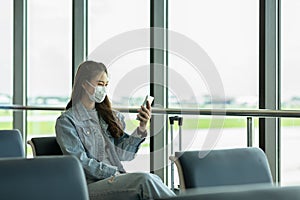 Asian young woman traveller wearing face maks using mobile phone at airport photo