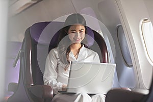 Asian young woman using laptop sitting near windows at first class on airplane during flight