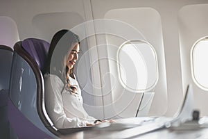 Asian young woman using laptop sitting near windows at first class on airplane during flight