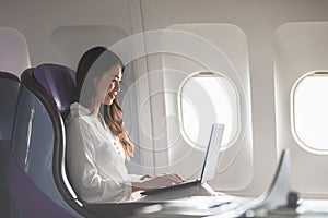 Asian young woman using laptop sitting near windows at first class on airplane during flight