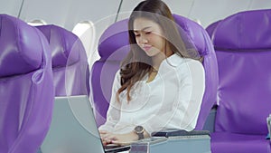 Asian young woman using laptop sitting near windows at first class on airplane during flight