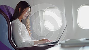 Asian young woman using laptop sitting near windows at first class on airplane during flight