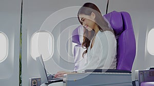 Asian young woman using laptop sitting near windows at first class on airplane during flight