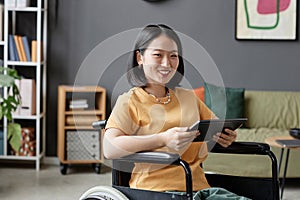 Asian young woman using wheelchair and holding tablet in office