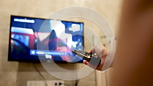 Asian young woman watching TV in the room with remote control in her hand to adjust volume or changing TV channel. Relaxation in l