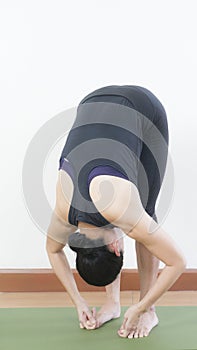 Asian young woman wear a black yoga outfit . Practicing yoga Standing Asanas Action PADANGUSTHASANA Big Toe pose .Home yoga