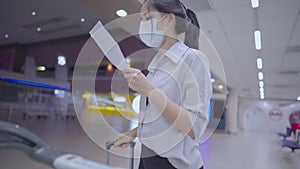 Asian Young woman wear face mask unfolding on ticket travel itinerary booking document paper, check on check-in time, lady travel