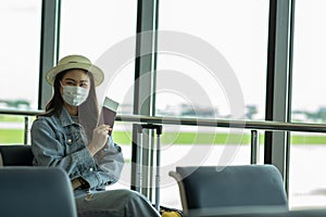 Asian young woman wearing face maks holding passport and boarding pass at airport Due Covid-19 flu virus pandemic