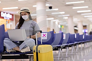 Asian young woman wearing face maks using laptop computer at airport Due Covid-19 flu virus pandemic