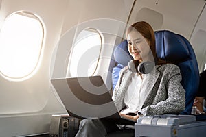 Asian young woman wearing headphone using laptop sitting near windows at first class on airplane during flight