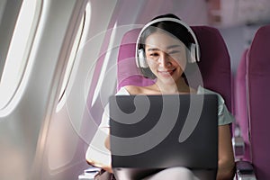 Asian young woman wearing headphone using laptop sitting near windows at first class on airplane during flight