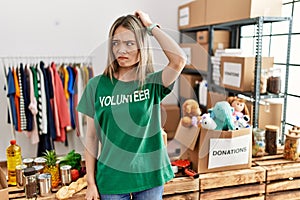 Asian young woman wearing volunteer t shirt at donations stand confuse and wondering about question