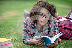 Asian young women and friends reading book on grass outside for education.