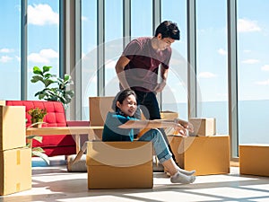 Asian young woman sitting in carton box while man come help before unpacking stuff for relocation new home