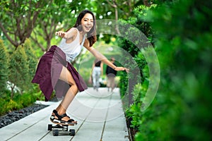 Asian young women surf skate or skates board outdoors on beautiful summer day. Happy young women play surf skate at park