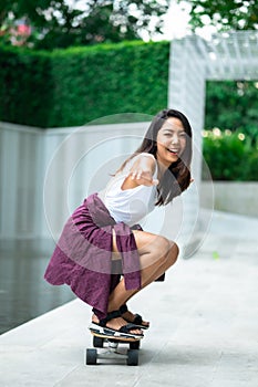 Asian young women surf skate or skates board outdoors on beautiful summer day. Happy young women play surf skate at park