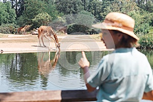 Asian zoology student girl looking at giraffe drinking from lake