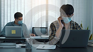 Asians sit in their office and use the phone to talk to clients while wearing masks in their offices during COVID-19