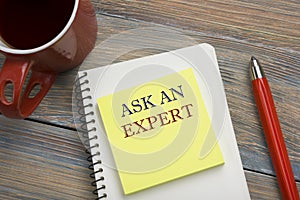 Ask an expert. Notepad with message, red pencil and coffee cup. Office supplies on desk table top view.