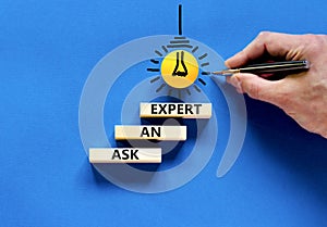 Ask an expert symbol. Concept words Ask an expert on wooden blocks on a beautiful blue table blue background. Yellow light bulb.