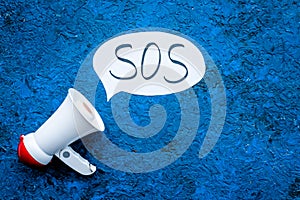 Ask for help concept. Megaphone near cloud with word SOS on blue background top view copy space