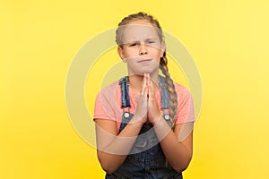 Ask permission. Portrait of imploring little girl in denim overalls holding hands in prayer gesture and pleading forgiveness