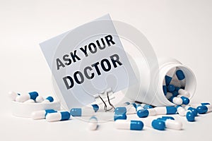 ASK YOUR DOCTOR, inscription on paper note near blue-white pills spilling out of pill bottle