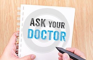 Ask your doctor word on white ring binder notebook with hand holding pencil on wood table,Health card concept