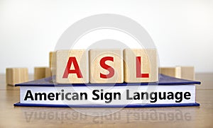 ASL, american sign language symbol. Wooden cubes on book with words `ASL, american sign language`. White background. Medical and