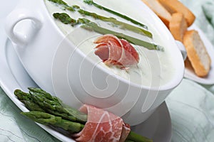 Asparagus soup with ham closeup in white bowl