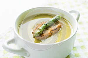 Asparagus soup in a white bowl with slice of bread and asparagus