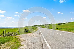 Asphalt long road crossing the green valley in a sunny summer day with bright blue sky