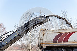 Asphalt milling and grinding machine at road repair and construction site throwing shredded old bitumen in big industrial heavy