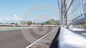 asphalt on a racing circuit with empty stands and iron guard rails, set against a green hill