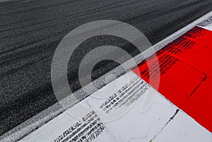 Asphalt red and white kerb of a race track detail with tire marks