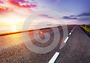 Asphalt road along the sea at sunset