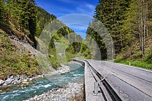 Asphalt road in Austria through the forest, valley in Austria in a beautiful summer day. Alps mountains tranquil summer view (