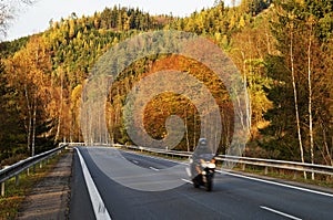 Asphalt road in the autumn landscape with a ride motorcycle, over the road forested mountain