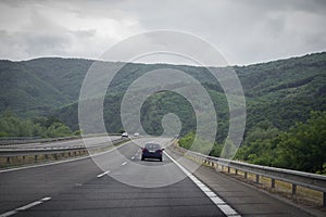 Asphalt road and car in the mountains with cloudy sky
