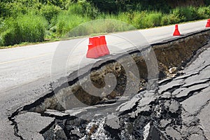 Asphalt road collapsed and cracks in the roadside - Road landslide subside with plastic barriers on uphill