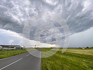 Asphalt road through the countryside farmland with dark storm clouds on horizon